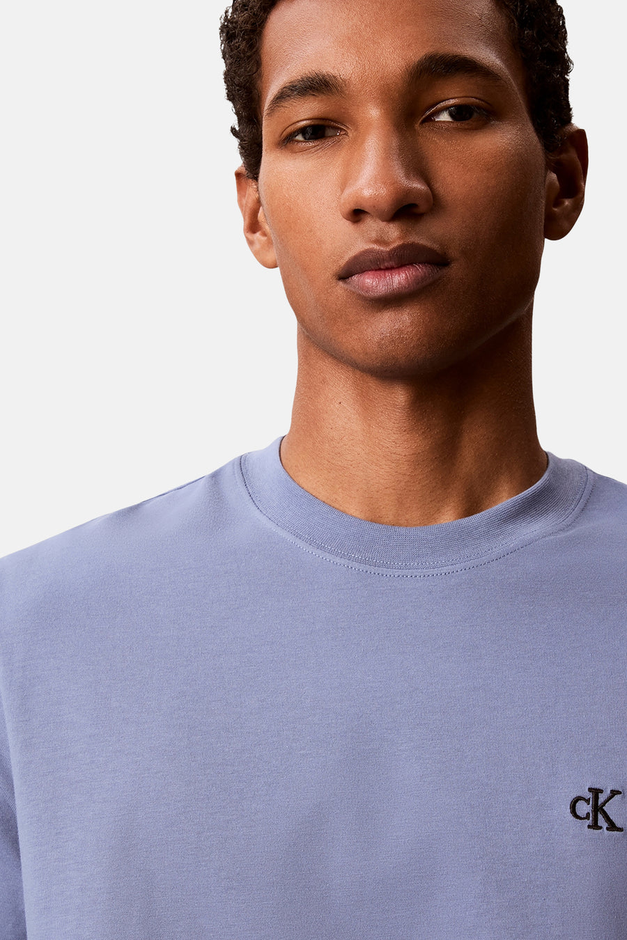 T-shirt lavande Calvin Klein avec logo CK brodé sur la poitrine, porté par un mannequin.