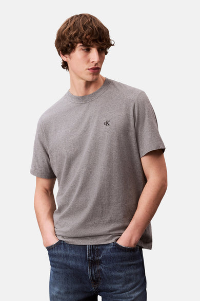 T-shirt gris à manches courtes de Calvin Klein, porté avec des jeans foncés et les mains dans les poches.