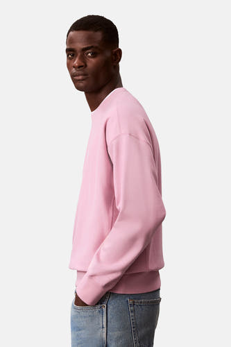 Pull-over rose de Calvin Klein, avec des manches longues et un col rond, porté avec des jeans en vue latérale.