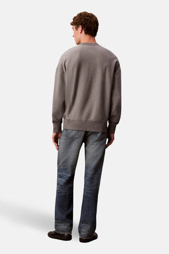 Pull gris Calvin Klein, avec des manches longues et porté avec des jeans bleus et des chaussures noires, vu de dos.