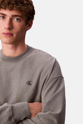 Pull gris Calvin Klein, avec un logo 'cK' brodé et des manches croisées.