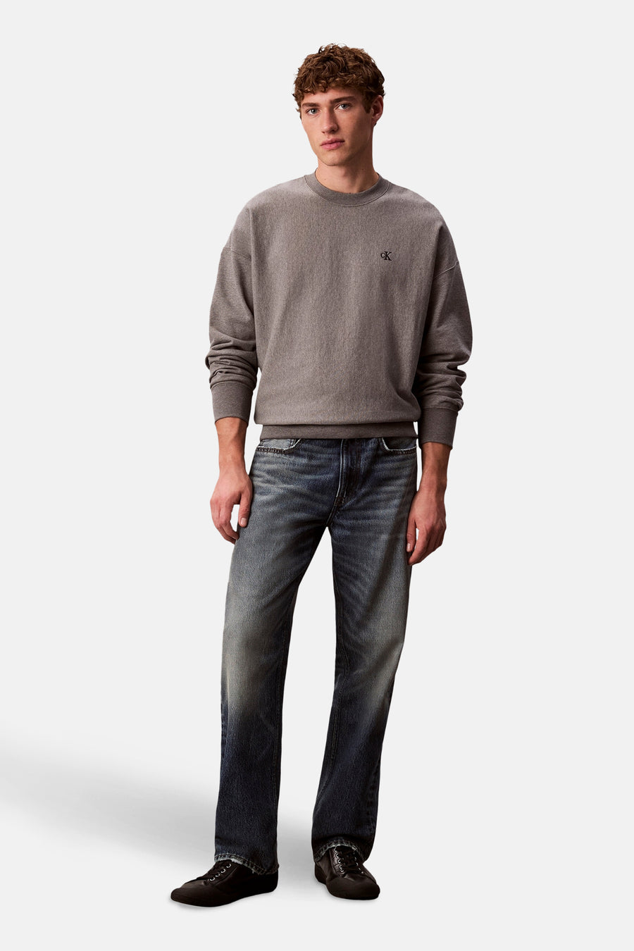 Een man met een grijze trui en blauwe jeans.