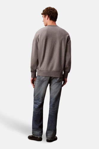 Pull-over gris avec col rond de Calvin Klein, avec des manches longues et associé à des jeans bleus et des chaussures noires.