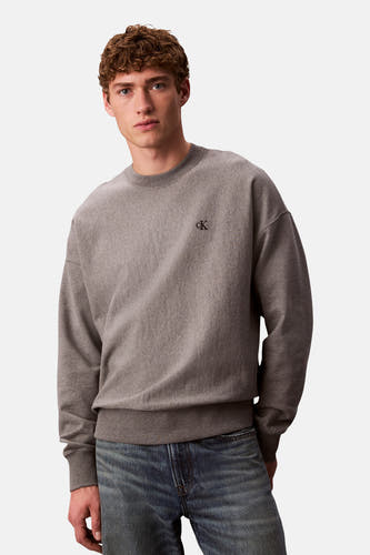 Grijze sweater van Calvin Klein, met een klein 'ck' logo op de borst, gedragen met een blauwe jeans.
