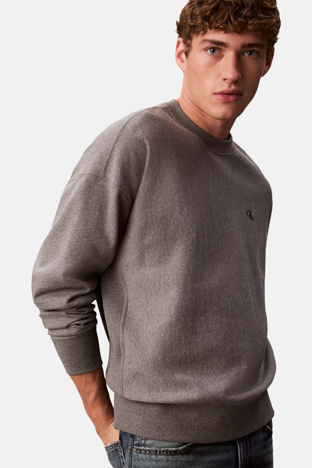 Pull-over gris Calvin Klein avec petit logo de la marque sur la poitrine, porté avec des jeans.