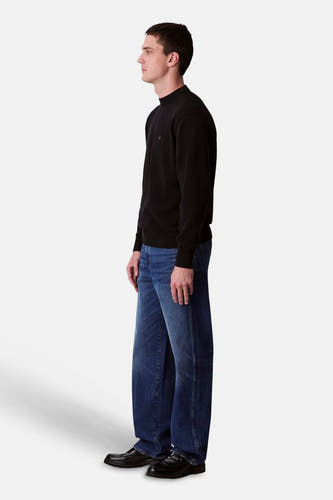 Pull-over noir de Calvin Klein avec des manches longues, associé à des jeans bleus et des chaussures noires, en vue latérale.