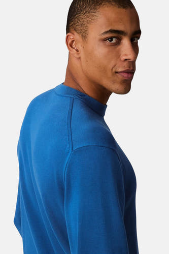Pull-over bleu de Calvin Klein, gros plan d'un homme qui regarde par-dessus son épaule.