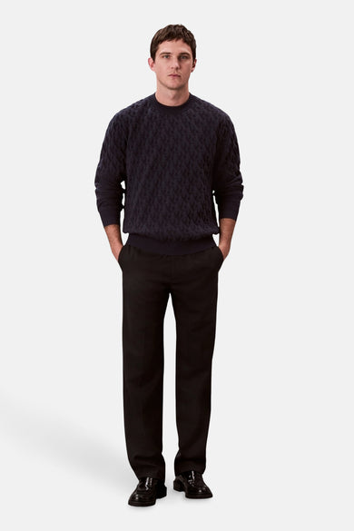 Pull-over bleu avec col rond de Calvin Klein, avec un motif en relief et porté avec un pantalon noir.