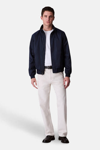 Veste de pluie bleue Calvin Klein portée avec un T-shirt blanc, un pantalon beige et des chaussures en cuir noires.