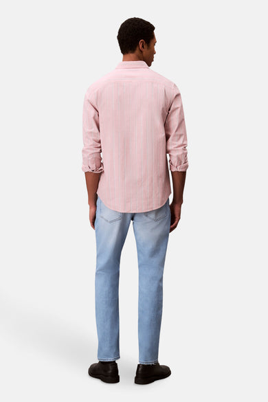 Jean slim de denim bleu clair de Calvin Klein, vu de de derrière, associé à une chemise rayée rose et des chaussures noires.