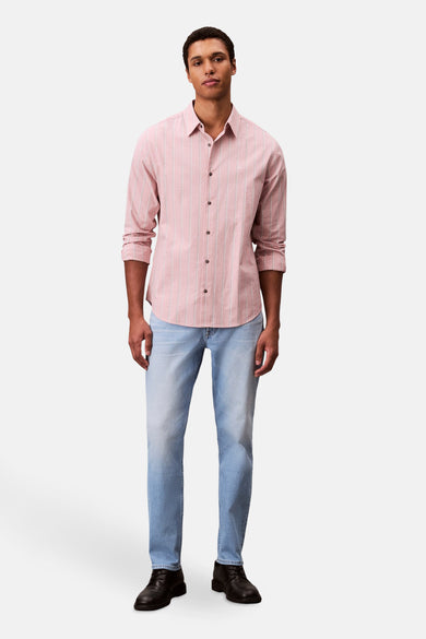 Jean slim en denim clair de Calvin Klein, associé à une chemise rayée et des chaussures noires.