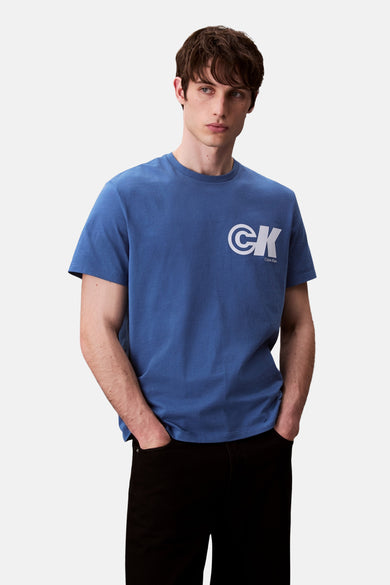T-shirt bleu à manches courtes de Calvin Klein, avec un logo CK blanc, associé à un pantalon noir.