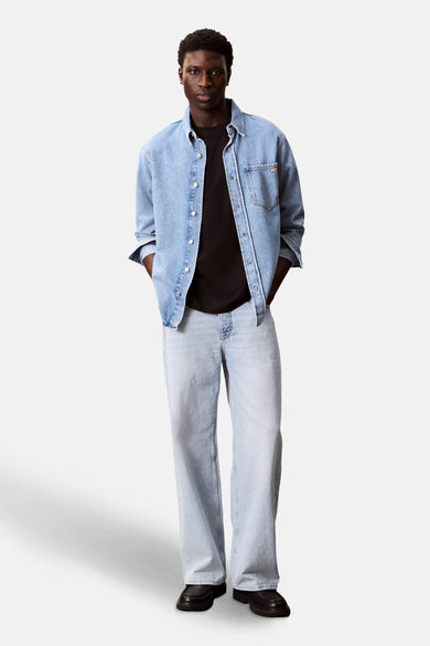 T-shirt noir à manches courtes de Calvin Klein, porté sous un chemisier denim bleu ciel ouvert avec des jeans larges.