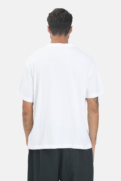 T-shirt blanc à manches courtes de Calvin Klein, vu de l'arrière, avec des tatouages sur les bras et un pantalon noir.
