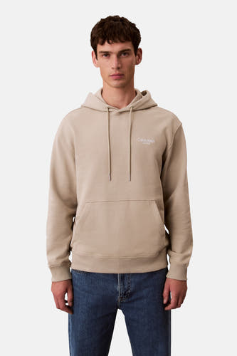 Gilet beige avec capuche de Calvin Klein Jeans, dos avec logo blanc, associé à un jean bleu marine.