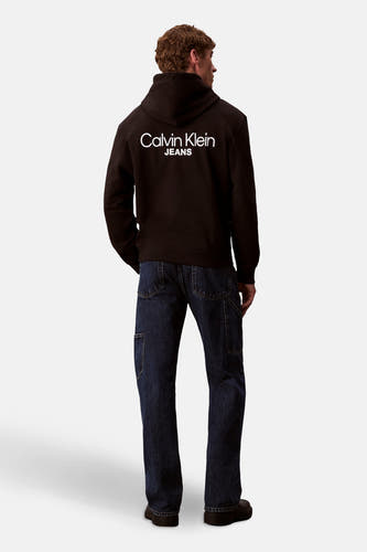 Pull-over noir avec capuche de Calvin Klein Jeans, vu de derrière, avec des jeans bleu marine et des chaussures noires.
