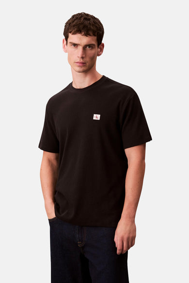 T-shirt noir à manches courtes de Calvin Klein, avec un petit logo sur la poitrine et porté avec des jeans foncés.