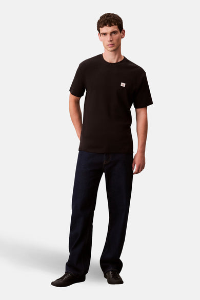 T-shirt noir à manches courtes de Calvin Klein, porté avec des jeans foncés et des chaussures noires.