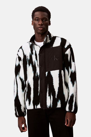 Short multicolored Calvin Klein jacket with black and white zebra pattern, black pants, and shoes.