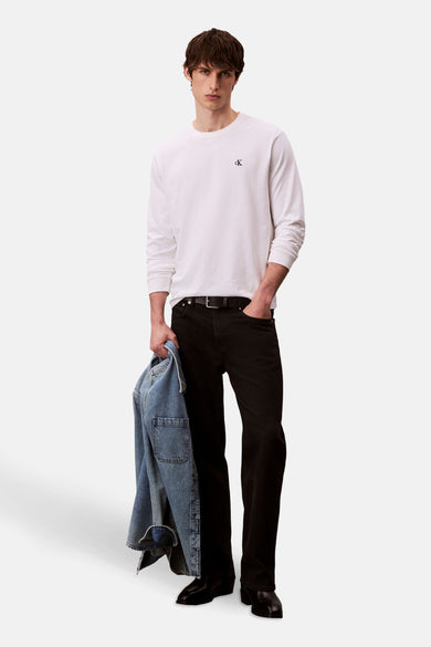 T-shirt blanc à manches longues de Calvin Klein, avec un petit logo CK sur la poitrine, porté avec des jeans noirs.