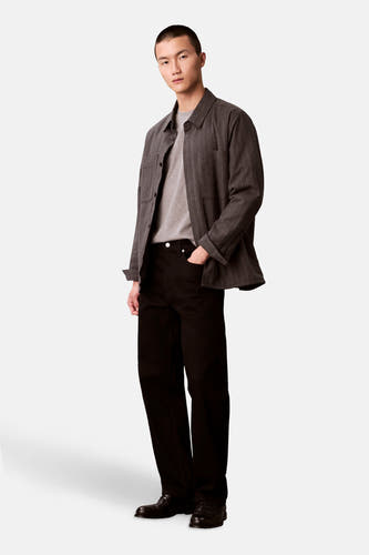 T-shirt gris à manches courtes de Calvin Klein, porté sous une chemise rayée et un pantalon noir.