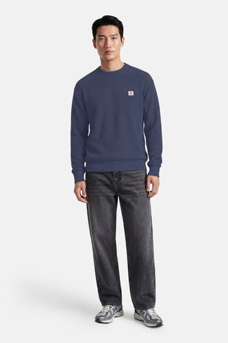 Blauwe ronde hals trui van Calvin Klein met wafeltextuur en klein logo op borst, gedragen met donkere jeans en sneakers, front view