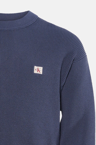 Blauwe ronde hals trui van Calvin Klein met fijne ribstructuur en klein wit logo op borst, close-up voorzijde