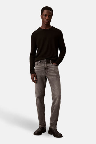 Jean slim Calvin Klein en denim gris moyen, porté avec un pull noir et des chaussures en cuir.