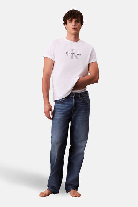 Rechte jeans van blauw denim van Calvin Klein, gedragen met een wit T-shirt en blote voeten.