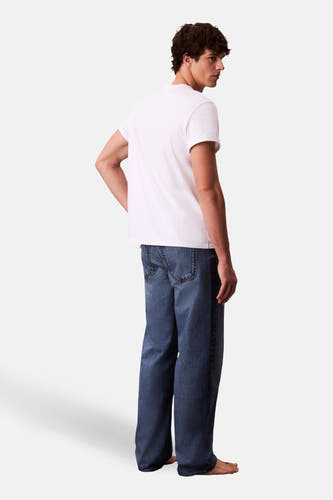 Jean droit bleu moyen en denim de Calvin Klein, avec jambes larges et un look décontracté, porté avec un t-shirt blanc.