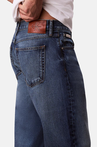 Jean bleu droit en denim, de Calvin Klein, avec étiquette en cuir marron et surpiqûres sur la poche arrière.