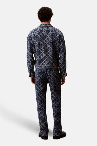 Blazer en denim bleu moyen de Calvin Klein, avec un imprimé logo sur toute la surface et des manches longues, vu de derrière.