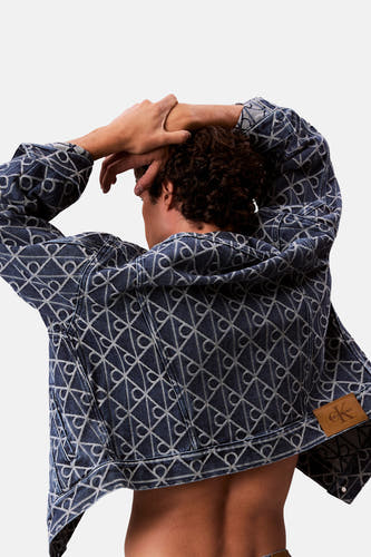 Manteau de denim bleu court de Calvin Klein, avec un motif de logos répétés sur le dos, porté par un modèle.