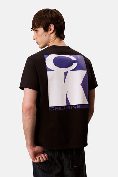 T-shirt noir à manches courtes de Calvin Klein, avec un grand imprimé blanc et bleu CK sur le dos.