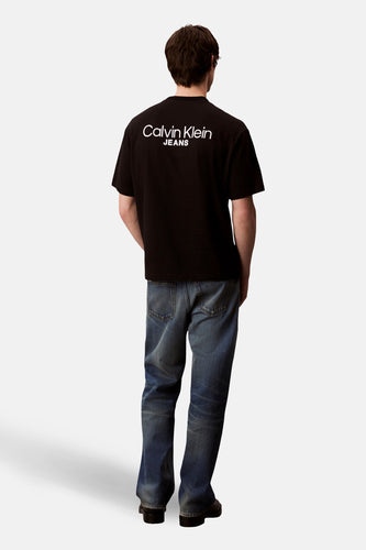 Zwart T-shirt met korte mouwen van Calvin Klein Jeans, met wit logo op de rug en blauwe jeans.
