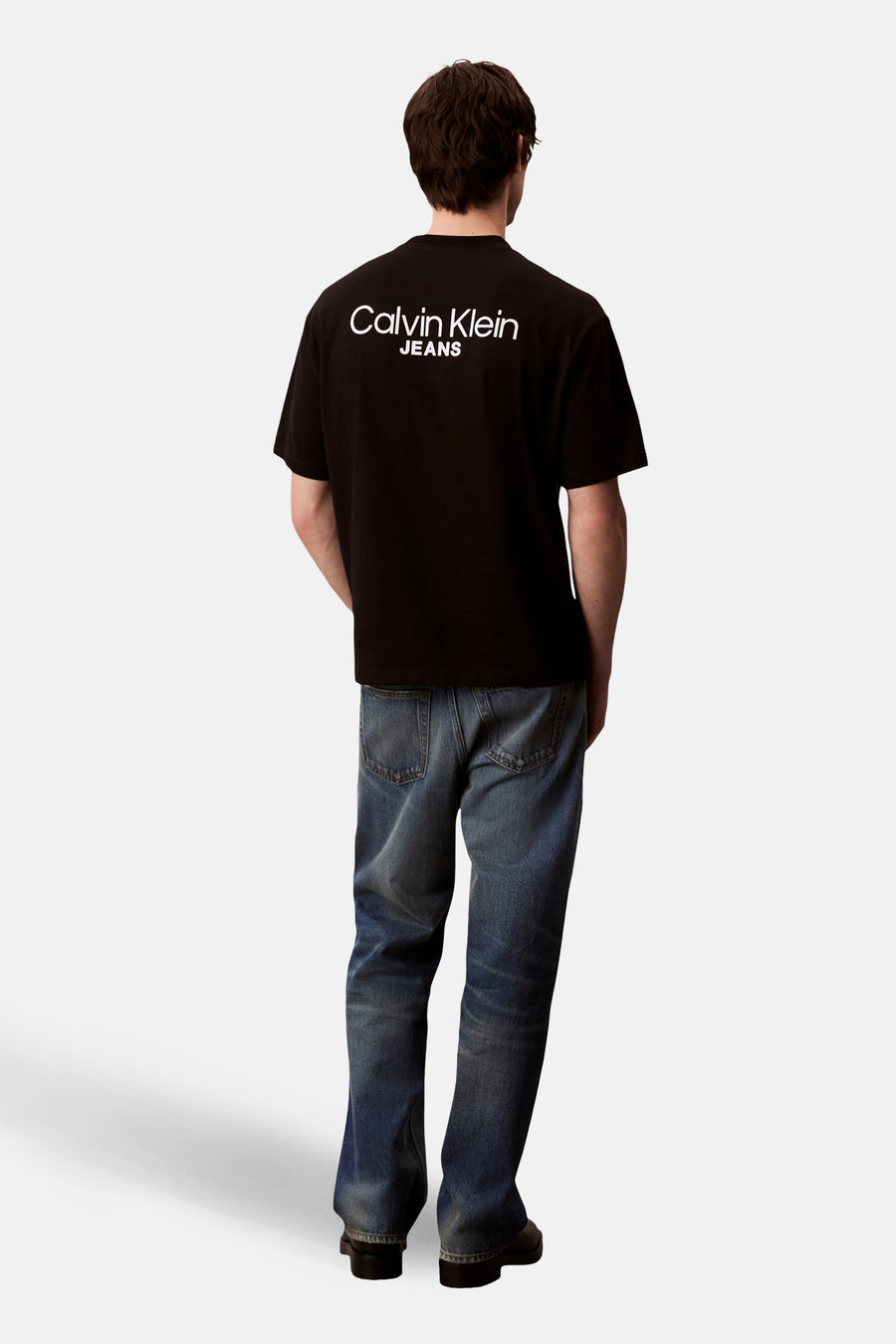 Zwart T-shirt met korte mouwen van Calvin Klein Jeans, met wit logo op de rug en blauwe jeans.
