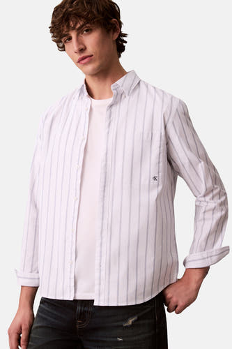 Blouse blanche à carreaux de Calvin Klein avec des manches longues, une poche poitrine et portée sur un T-shirt blanc, associée à un jean.