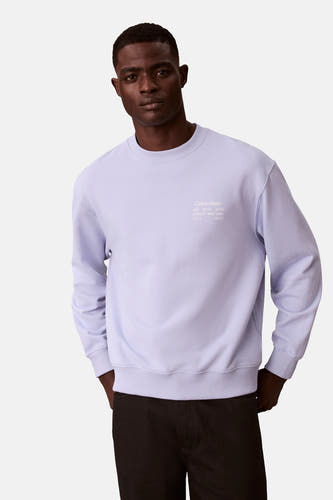 Pull-over marron Calvin Klein avec imprimé sur le dos, porté avec un pantalon noir.