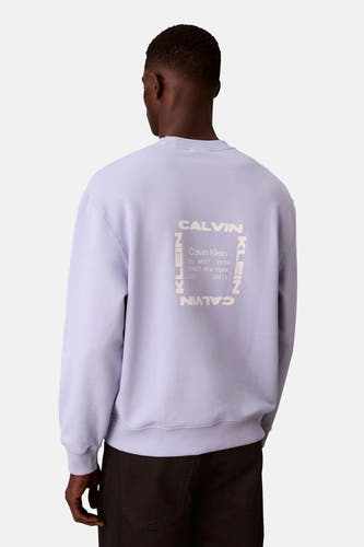 Paarse sweater van Calvin Klein met print op de achterkant, gedragen met een zwarte broek.

