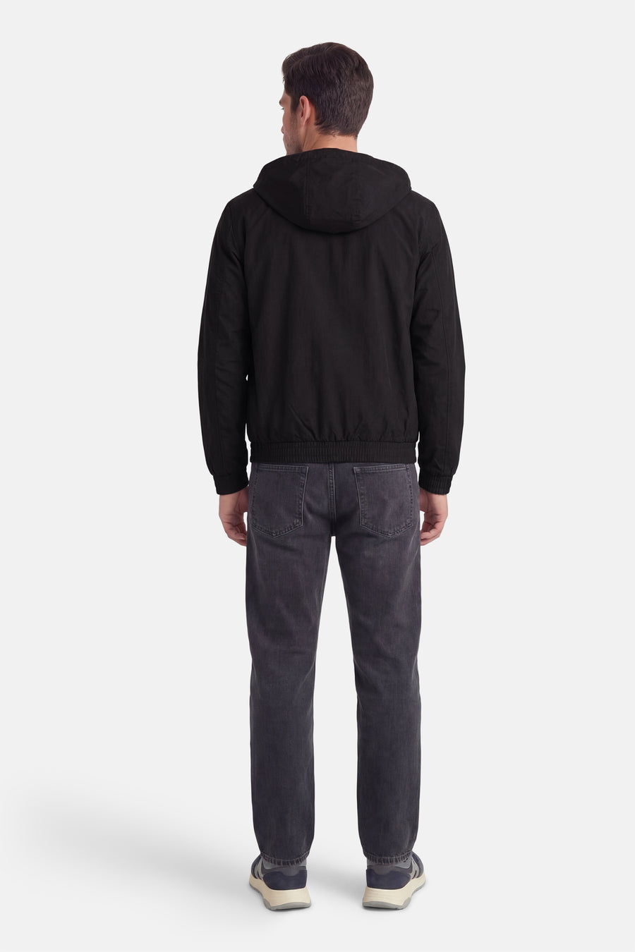Zwarte regenjas van Calvin Klein, gezien van achteren, met capuchon en donkere jeans met schoenen.