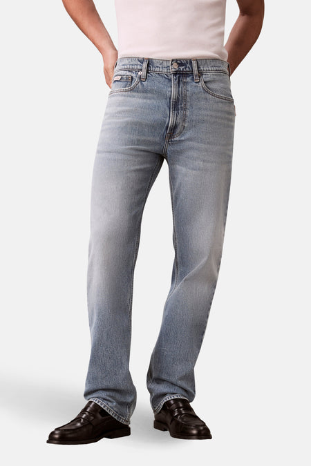 Jeans straight lichtblauwe denim van Calvin Klein, gecombineerd met zwarte leren loafers en een wit hemd.