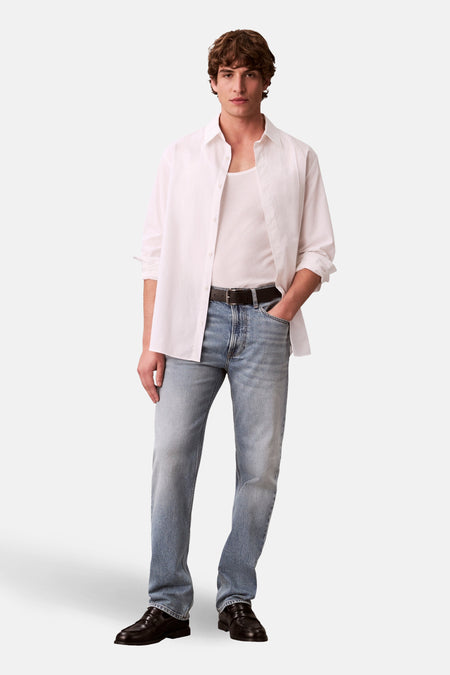 Rechte jeans van lichtblauw denim van Calvin Klein, met een zwarte riem, gecombineerd met een wit shirt.