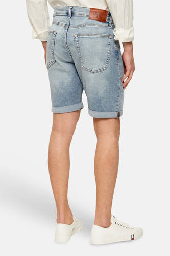 Short en jean bleu clair Calvin Klein avec ourlets retroussés et poches arrière visibles, associé à une chemise blanche et des baskets blanches.