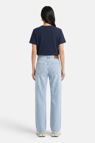 Lichtblauwe straight jeans van Calvin Klein, achterzijde, met bruin label en rechte pijpen, gedragen met donkerblauw T-shirt en witte sneakers.