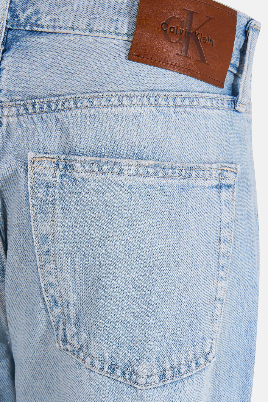Lichtblauwe straight jeans van Calvin Klein met bruin leerlabel en gewassen denimtextuur, close-up van achterzak