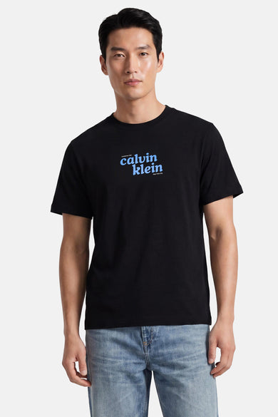 Zwart korte mouwen T-shirt van Calvin Klein met blauw logo op borst, gedragen door model in lichtblauwe jeans, front view