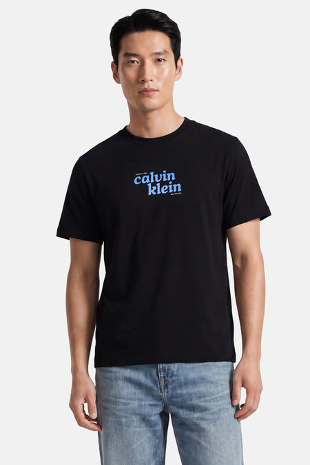 Zwart korte mouwen T-shirt van Calvin Klein met blauw logo op borst, gedragen door model in lichtblauwe jeans, front view