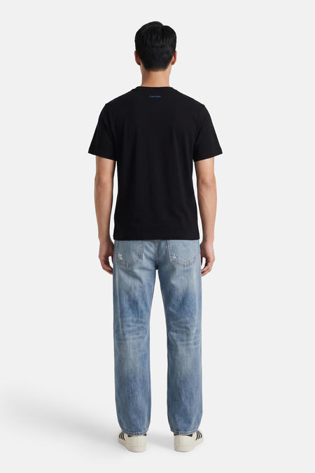 Zwart korte mouwen T-shirt van Calvin Klein, achterzijde met klein logo, gedragen met lichtblauwe jeans en witte sneakers