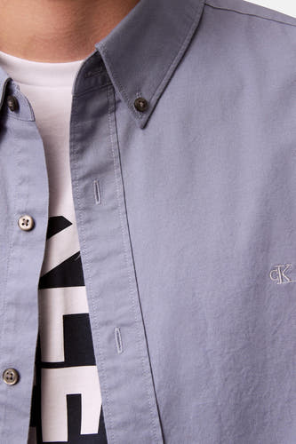Chemise bleue à longues manches de Calvin Klein, avec un T-shirt blanc en dessous et un petit logo.