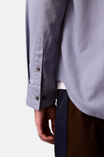 Chemise bleue à manches longues de Calvin Klein, montrée avec des boutons de manchette et un pantalon bleu marine avec des taches brunes.